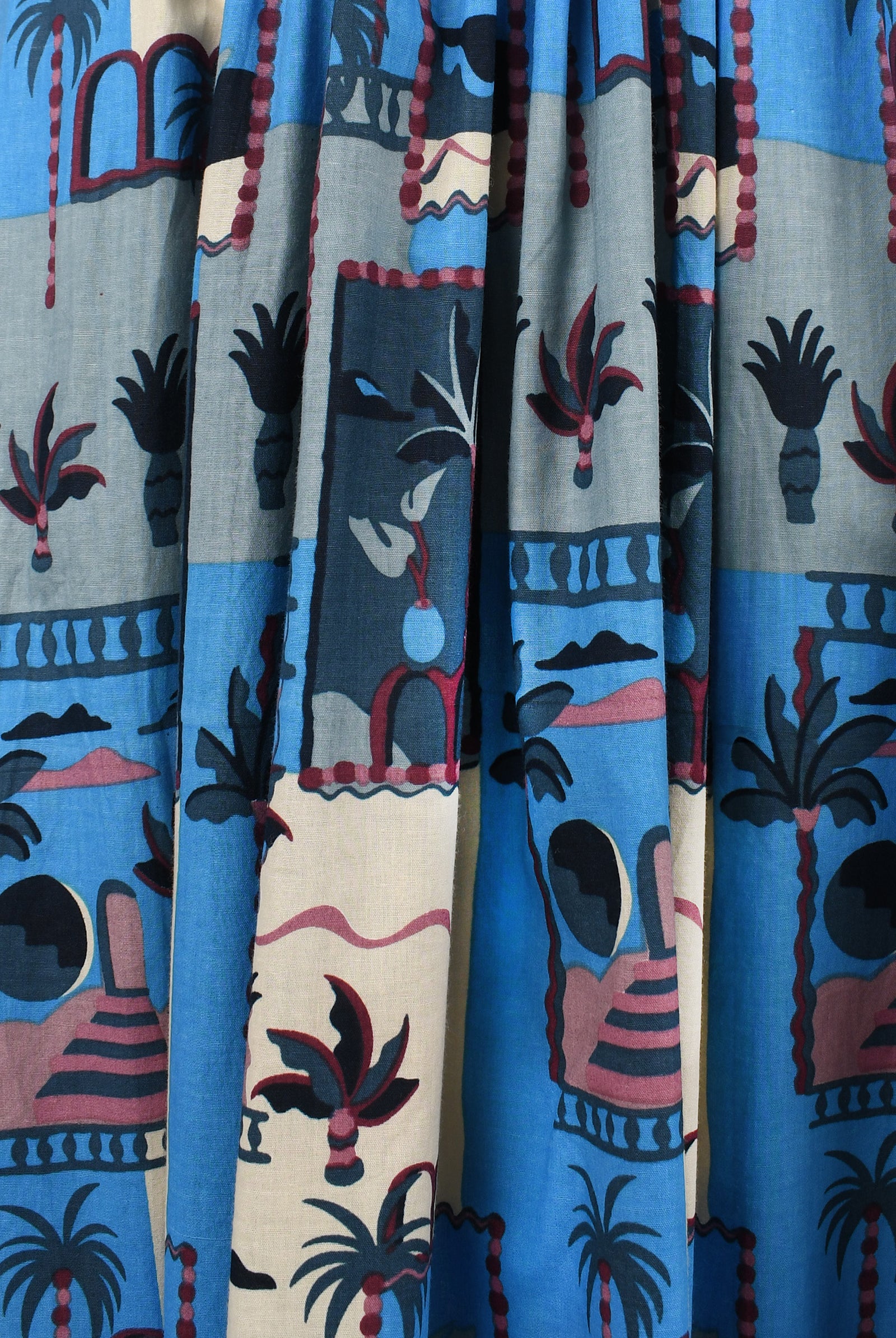 Close-up of blue-and-cream illustrated fabric with palm trees, houses, and animals