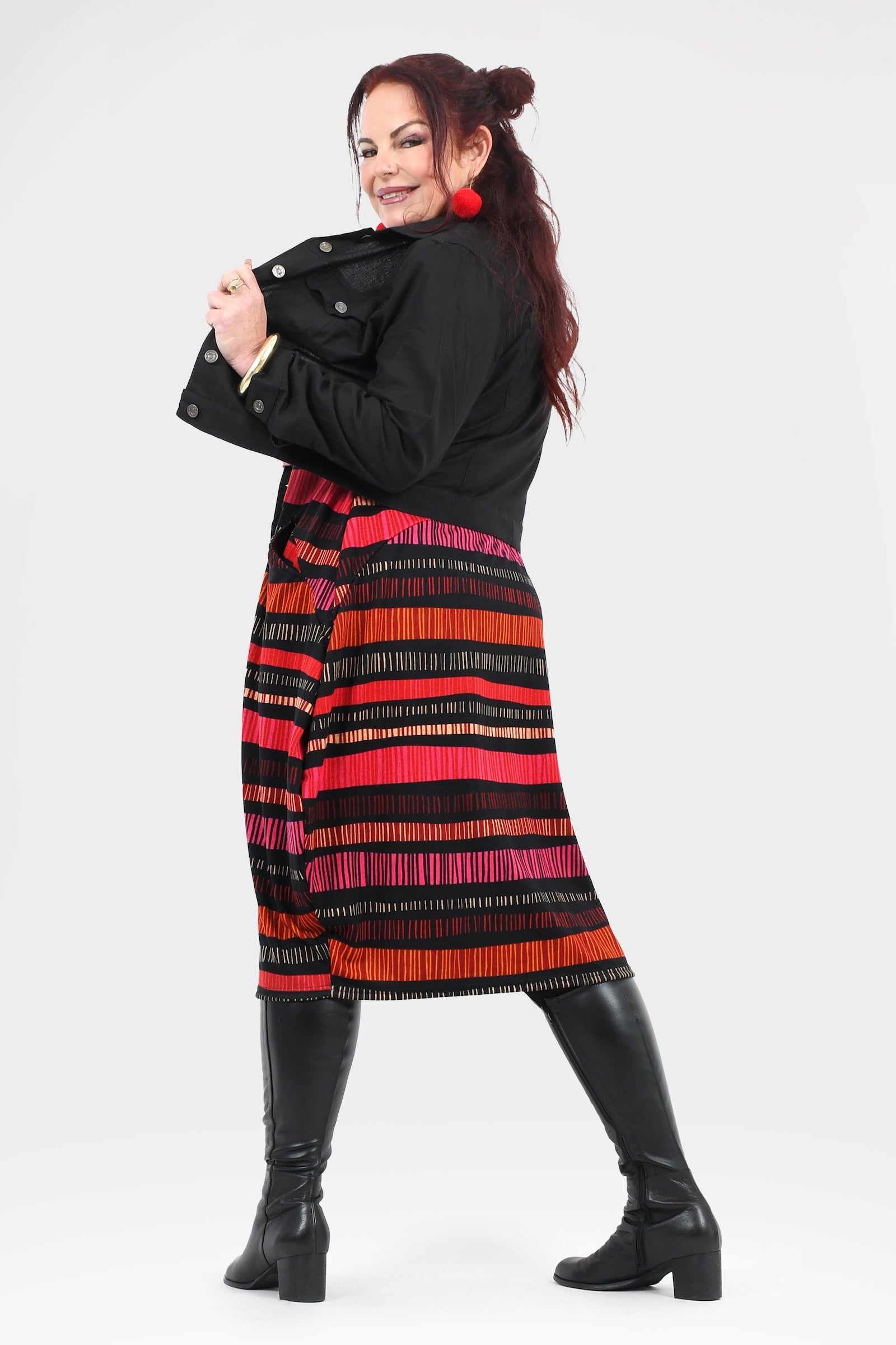 Woman wearing a black coat with a colorful striped dress underneath on a white background