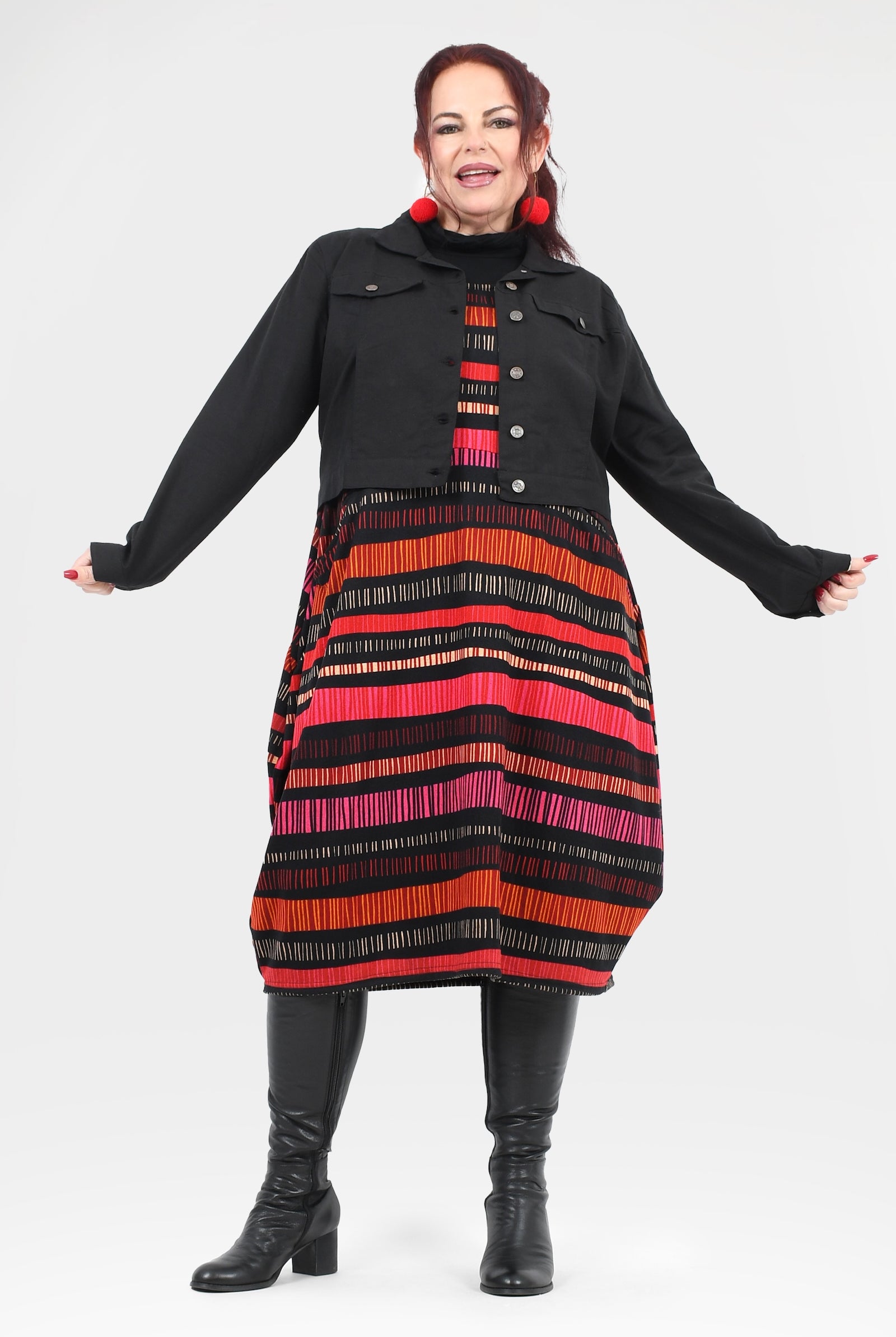 Woman wearing a black coat with a colorful striped dress underneath on a white background