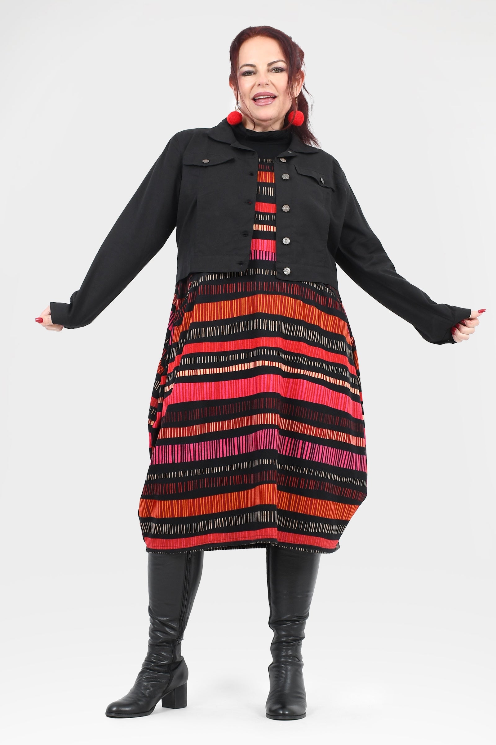 Woman wearing a black coat with a colorful striped dress underneath on a white background