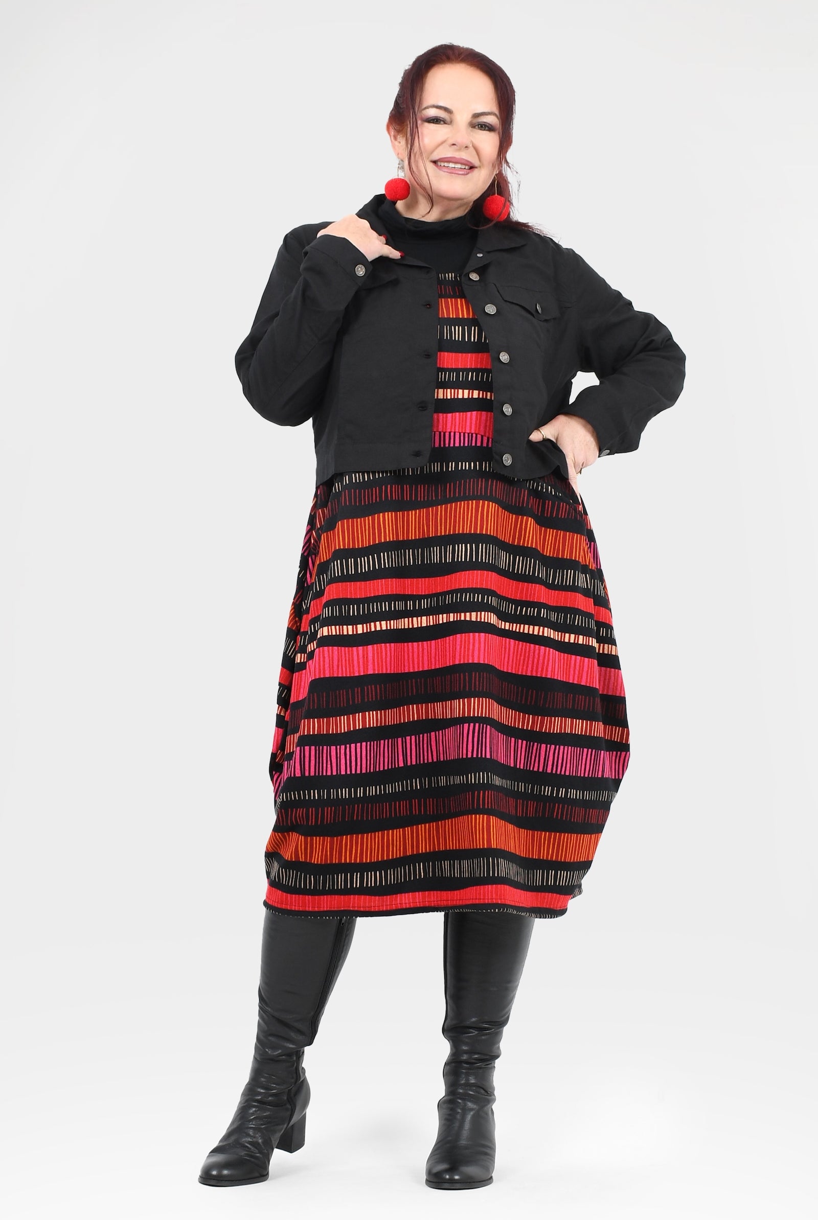 Woman wearing a black coat over a colorful striped dress on a white background