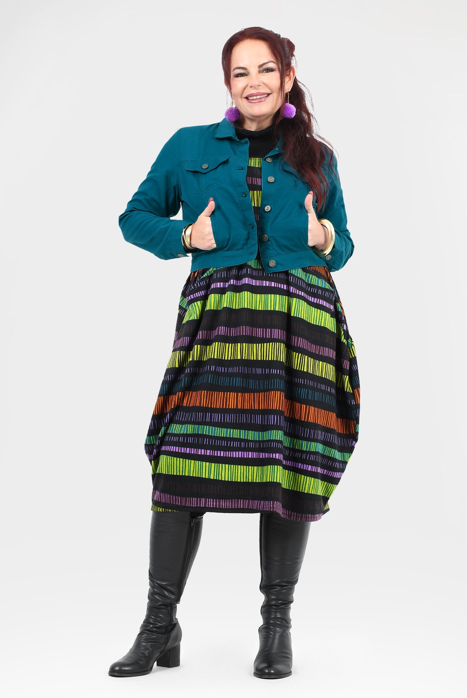 Woman wearing a colorful striped dress with a teal jacket on a white background