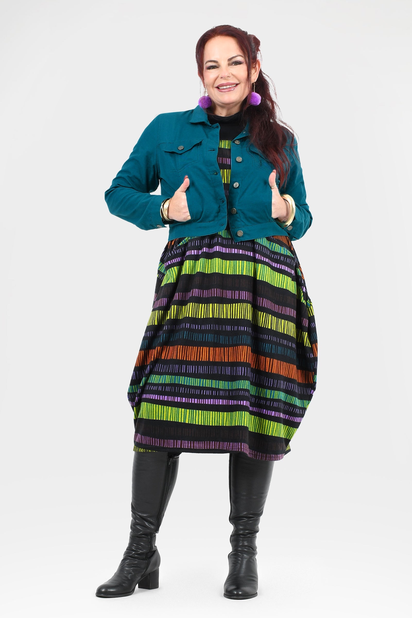 Woman wearing a colorful striped dress with a teal jacket on a white background