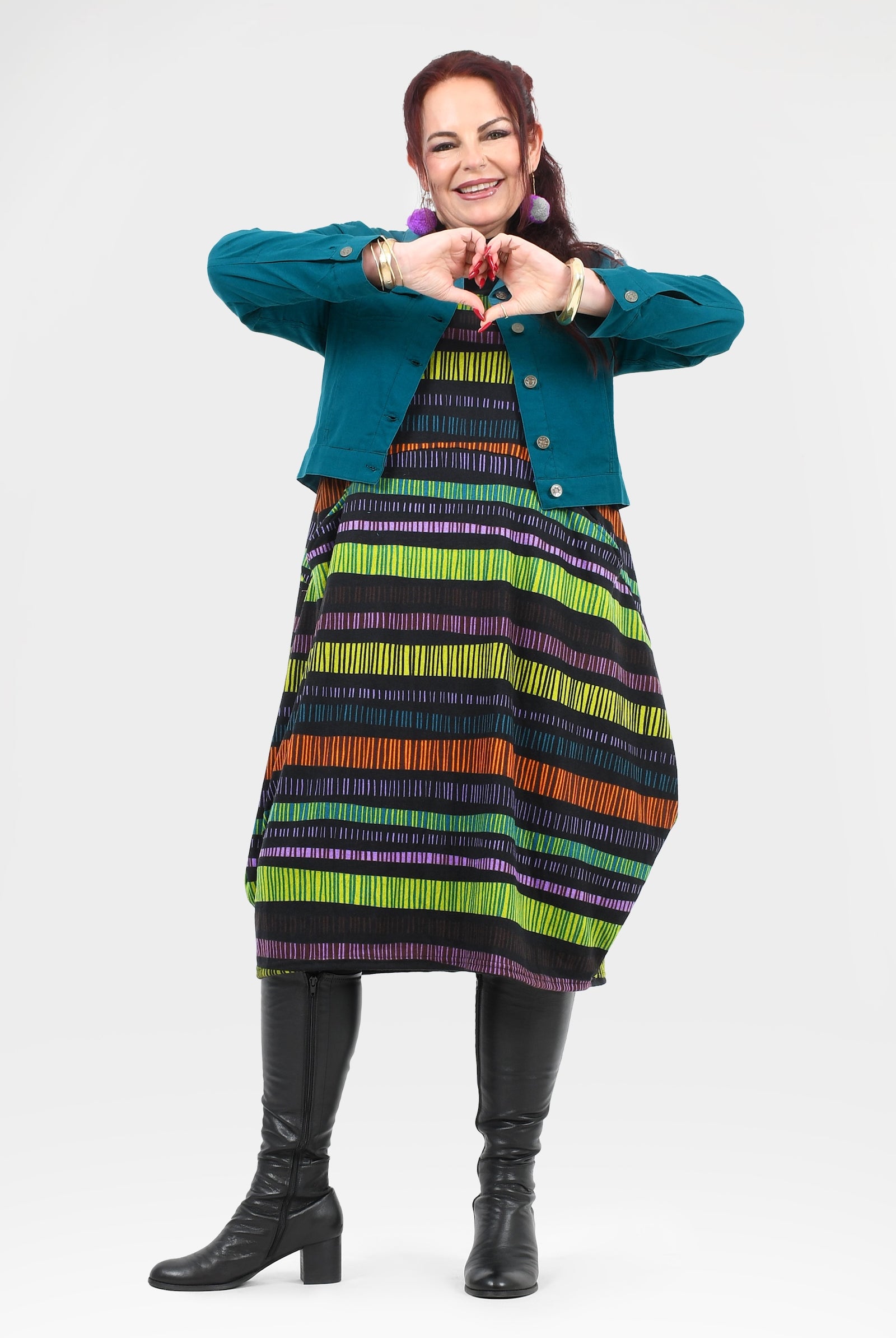 Woman wearing a colorful striped dress and teal jacket on a white background