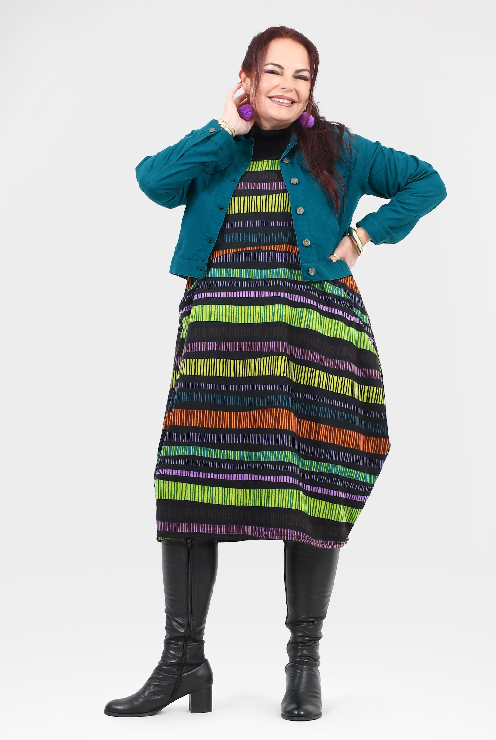 Woman wearing a colorful striped dress with a teal jacket on a white background