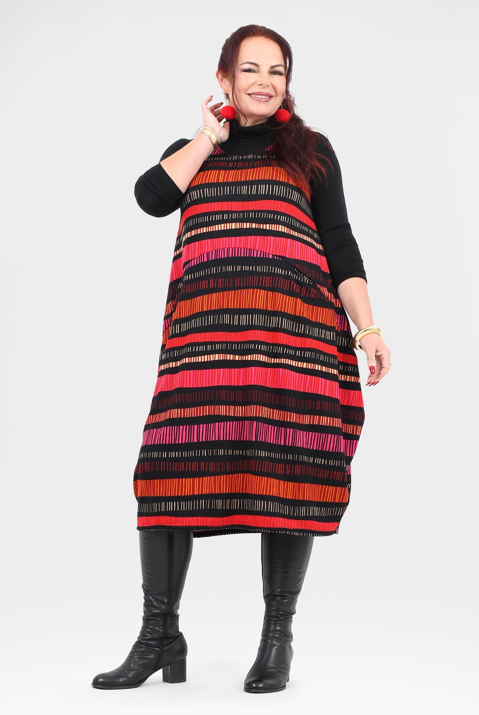 Woman wearing a colorful striped dress with a black turtleneck and black boots on a white background