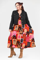 Woman wearing a colorful dress with geometric patterns and a black jacket on a white background