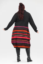 Person wearing a black cardigan over a colorful striped dress on a white background