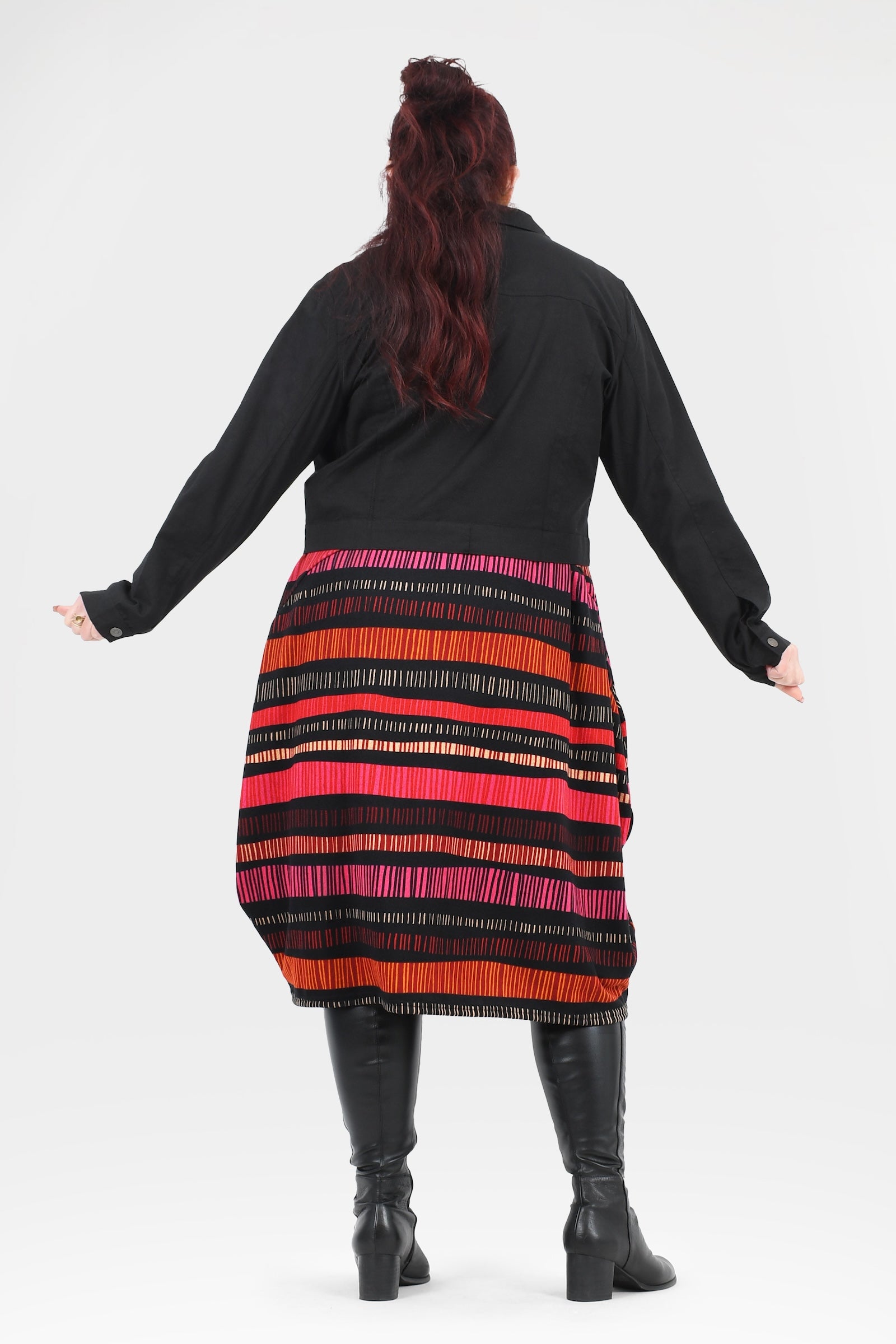 Person wearing a black cardigan over a colorful striped dress on a white background