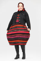 Woman wearing a black coat over a colorful striped dress on a white background