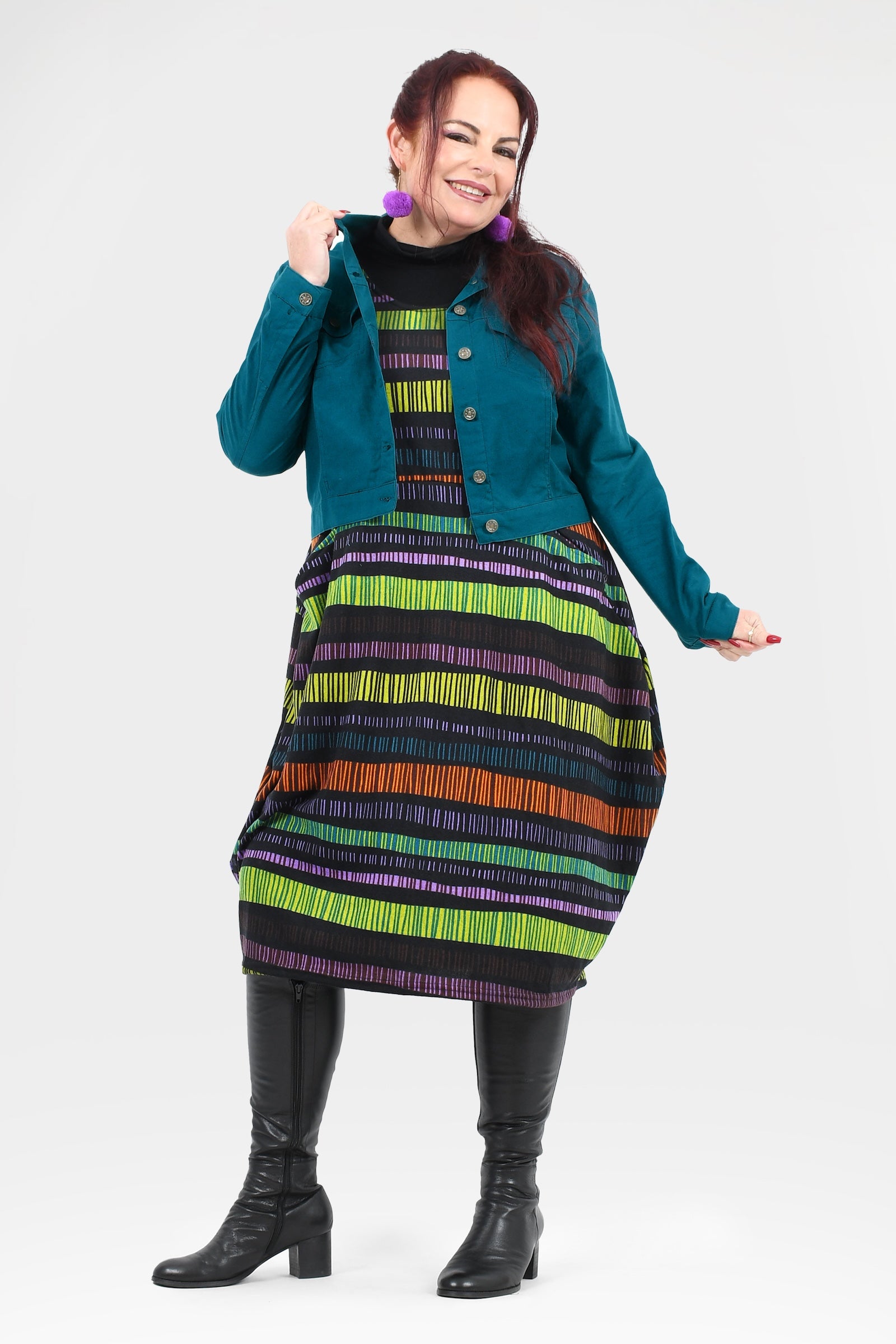 Woman wearing a teal jacket over a colorful striped dress on a white background