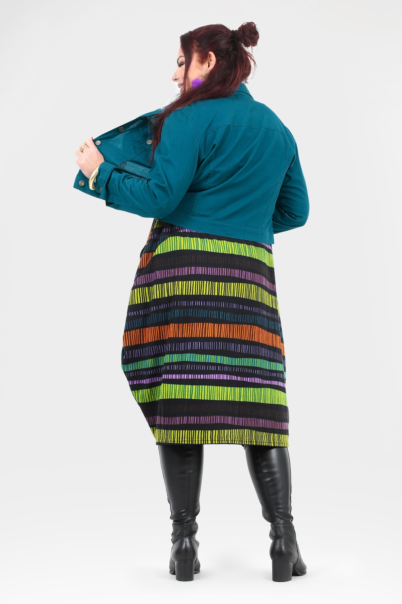 Person wearing a teal jacket and colorful striped skirt on a white background