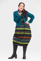 Woman wearing a colorful striped dress with a teal jacket on a white background