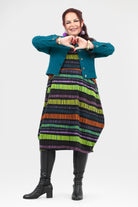 Woman wearing a colorful striped dress and teal jacket on a white background