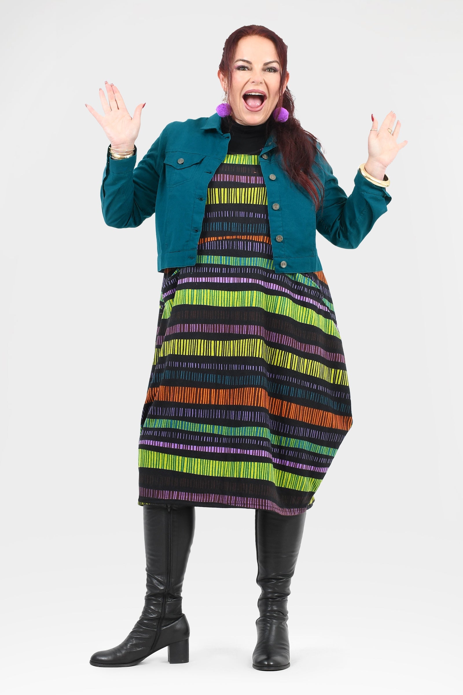 Woman wearing a colorful striped dress with a teal jacket on a white background