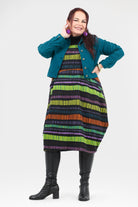 Woman wearing a colorful striped dress with a teal jacket on a white background