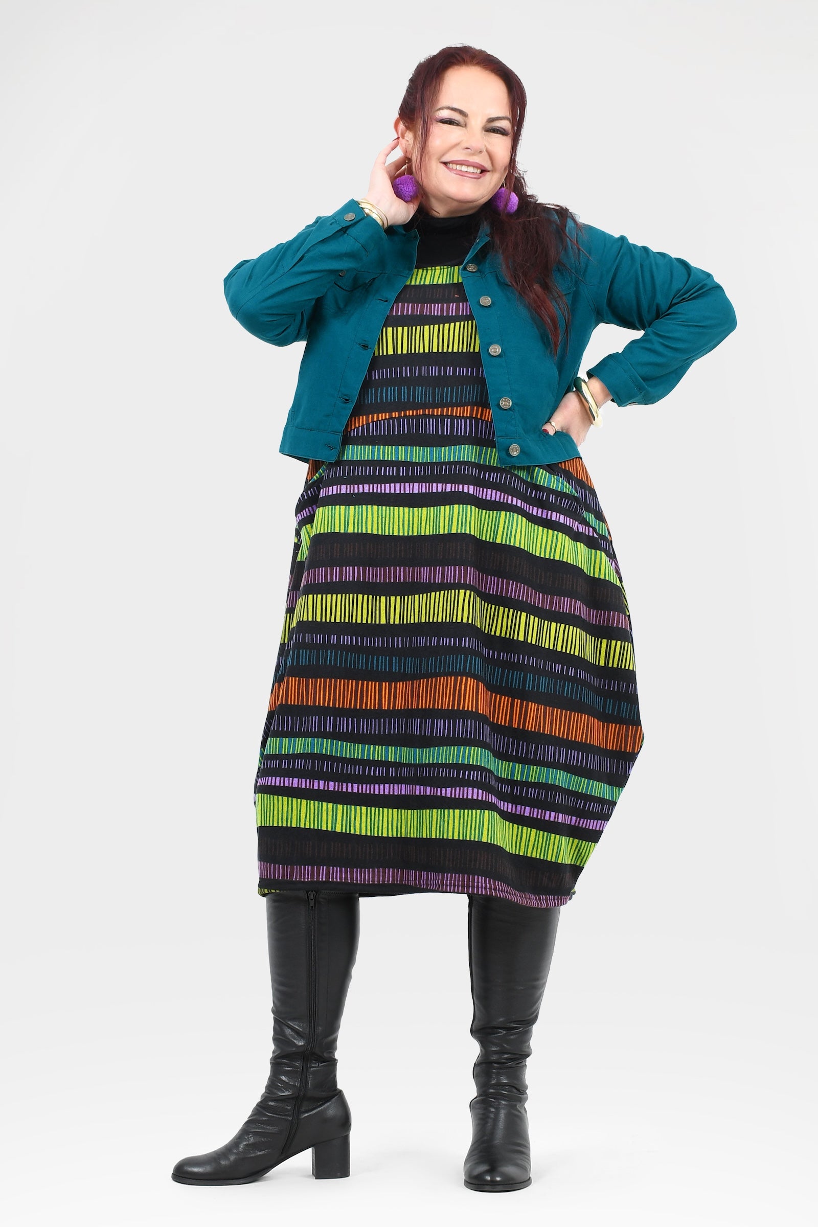Woman wearing a colorful striped dress with a teal jacket on a white background