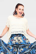 Cream popcorn knit top with wide neckline and fringe across chest