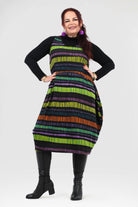 Woman wearing a colorful striped dress with a black turtleneck and boots on a white background