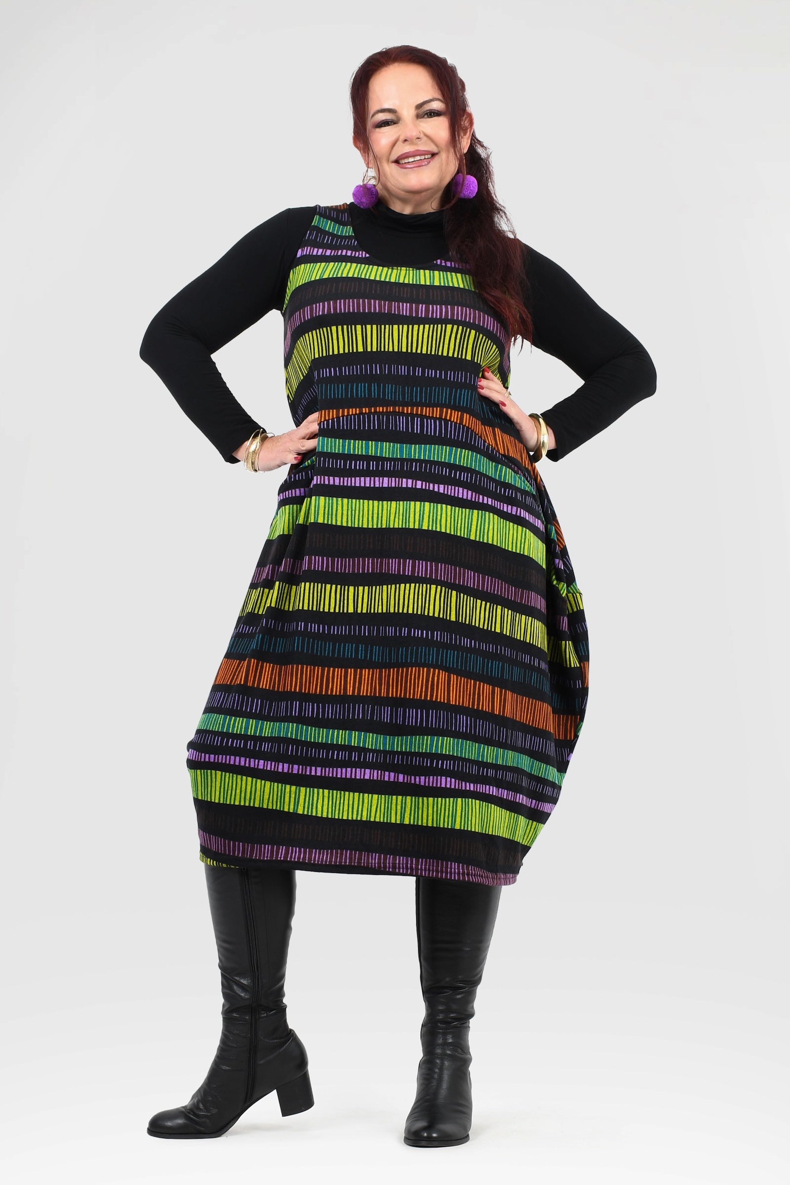 Woman wearing a colorful striped dress with a black turtleneck and boots on a white background